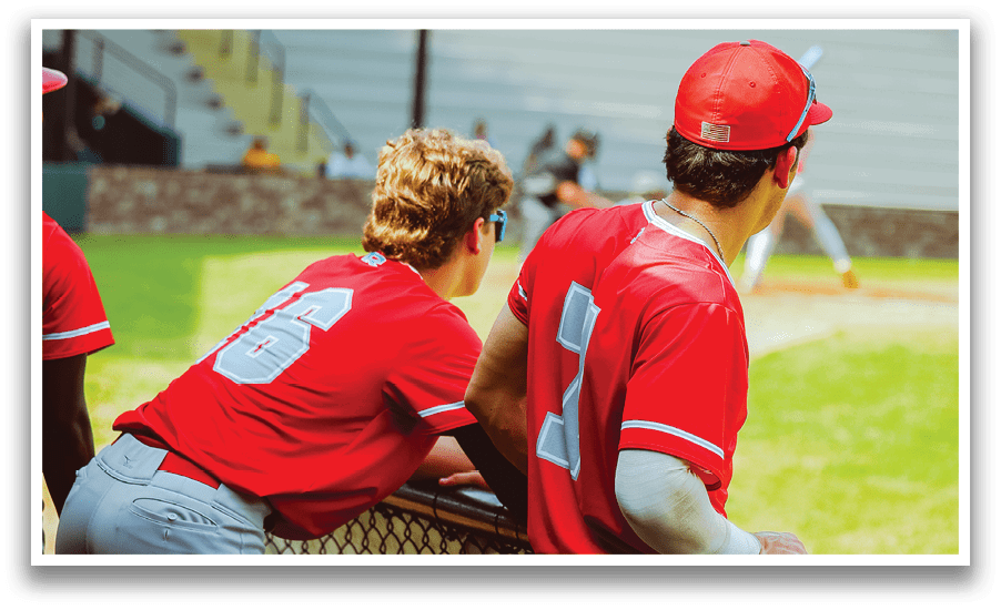 Two baseball players wearing red jerseys are leaning on a fence, watching the game. AI generated content
