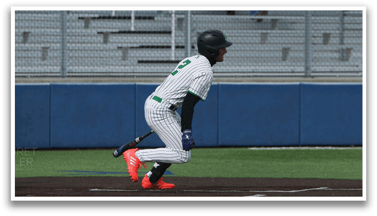 A baseball player is at bat, wearing a green and white uniform. The player is holding a baseball bat and is ready to swing. There are several other people in the scene, some of whom are sitting on a bench. AI generated content