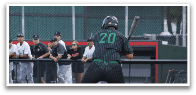 A baseball player in a green shirt and black pants is swinging a bat. Description generated by AI