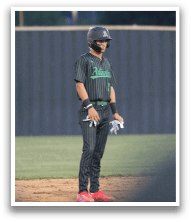 A baseball player wearing a green shirt and black pants stands on the field. Description generated by AI