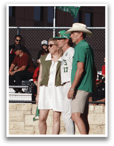 A man wearing a green shirt and a green hat is talking to a baseball player. Description generated by AI