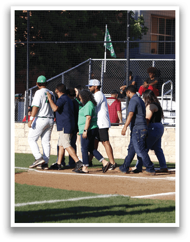A man wearing a green shirt and a green hat is talking to a baseball player. Description generated by AI