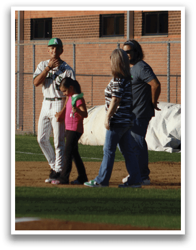 A man wearing a green shirt and a green hat is talking to a baseball player. Description generated by AI