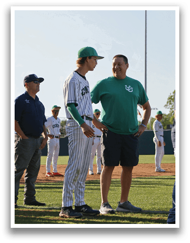 A man wearing a green shirt and a green hat is talking to a baseball player. Description generated by AI