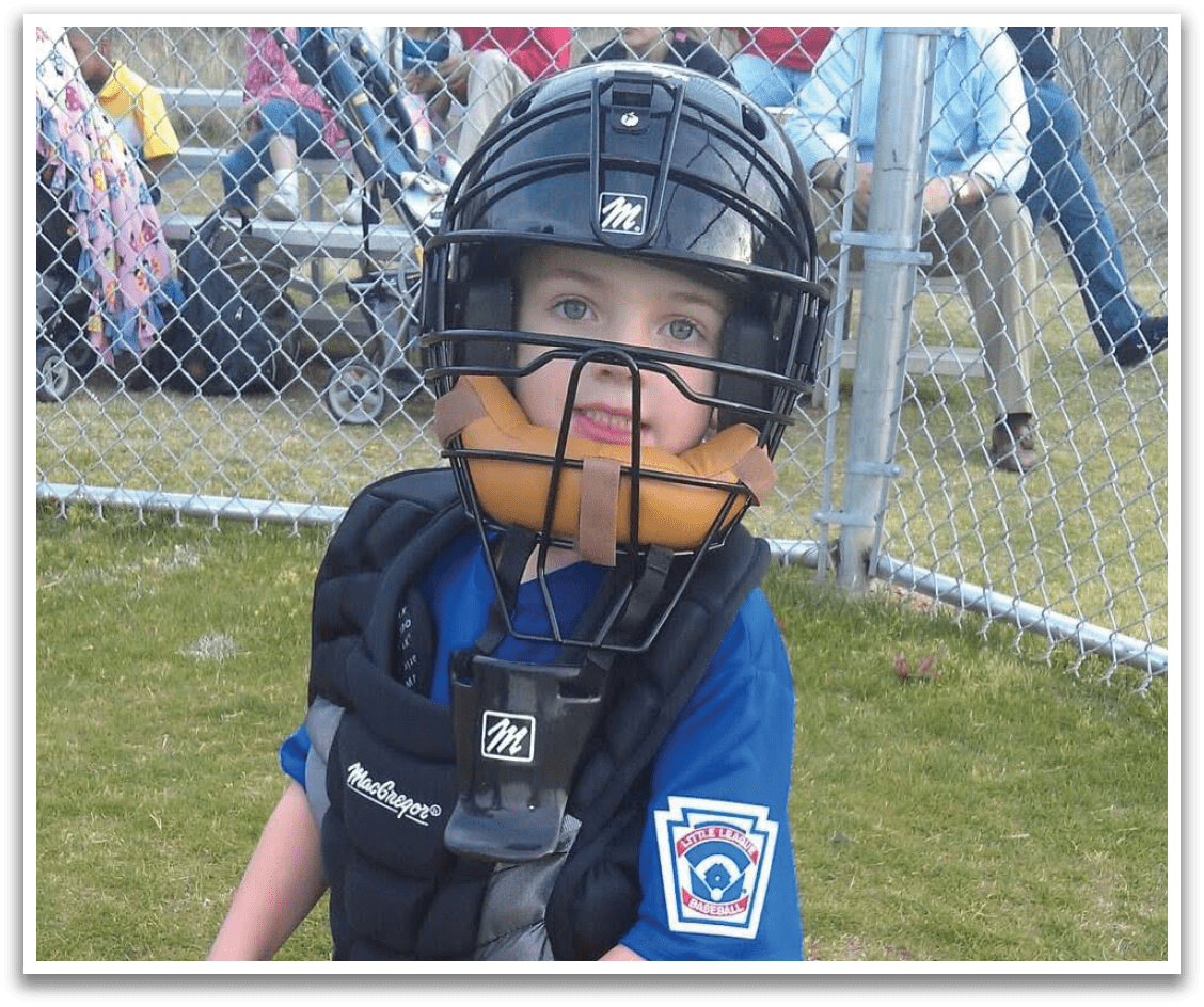 A young boy wearing a catcher's mitt and chest protector. Description generated by AI