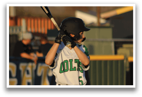 A young boy in a white baseball uniform is standing at home plate, holding a bat and waiting for the pitch. AI generated content