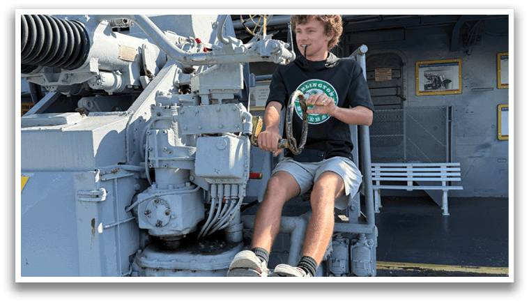 A young boy is sitting on a large gun turret, holding a can of soda. AI generated content