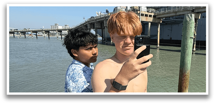 Two people are standing on a dock, one of them is taking a picture of the other using a cell phone. AI generated content