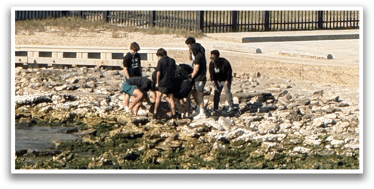 A group of people are standing near a body of water, with some of them wearing bathing suits. AI generated content