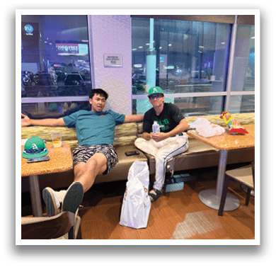 Two men are sitting at a table in a restaurant, enjoying their time together. They have drinks in front of them, and one of them is holding a bottle. There are also a few chairs around the table, and a dining table in the background. AI generated content