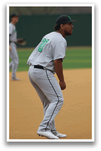 A baseball player wearing a green shirt and white pants is standing on the field. AI generated content
