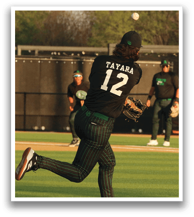 A baseball player in a black shirt and green pants is throwing a ball on a field. AI generated content