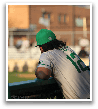 A baseball player wearing a green hat and white uniform sits on a fence. AI generated content