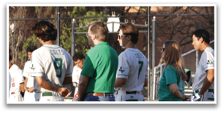 A group of baseball players are standing on the field, some of them wearing green and white uniforms. They are gathered near the dugout, possibly waiting for their turn to play or discussing the game. AI generated content