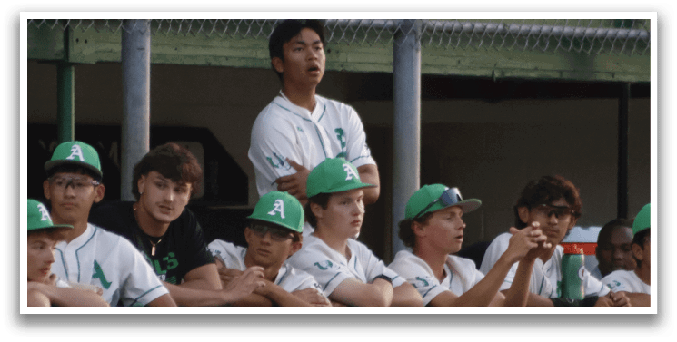 A group of young men are sitting on a bench, watching a baseball game. AI generated content