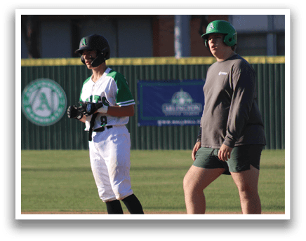 A baseball player wearing a green and white uniform stands on the field holding a baseball bat. Another person, possibly a coach, stands nearby. AI generated content