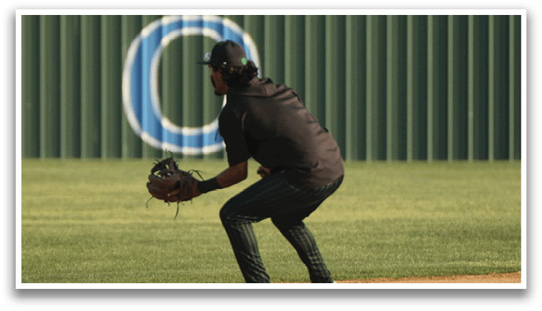 A baseball player in a black shirt and green pants is catching a ball. Description generated by AI