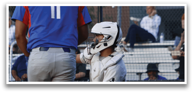 A baseball player wearing a blue shirt and red hat bends over to talk to a catcher. Description generated by AI