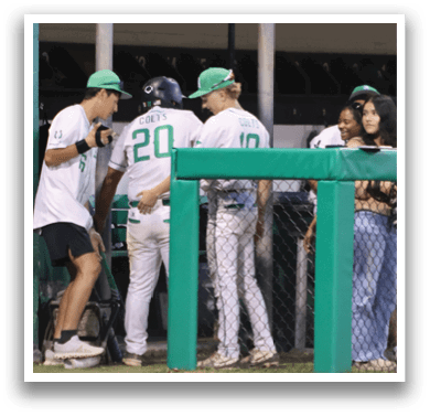 A group of people standing in front of a green fence. Description generated by AI