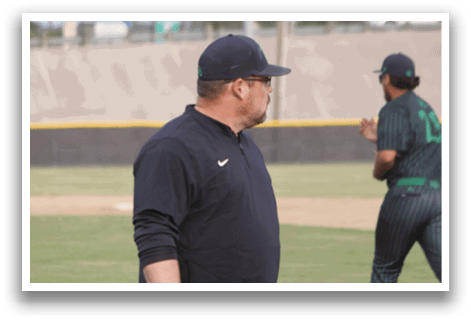 A man wearing a black shirt and green pants standing on a baseball field. Description generated by AI