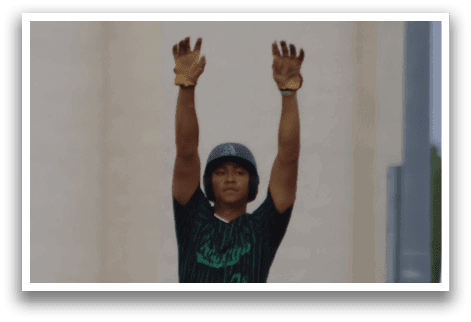 A baseball player wearing a green and black uniform is standing on a field. Description generated by AI