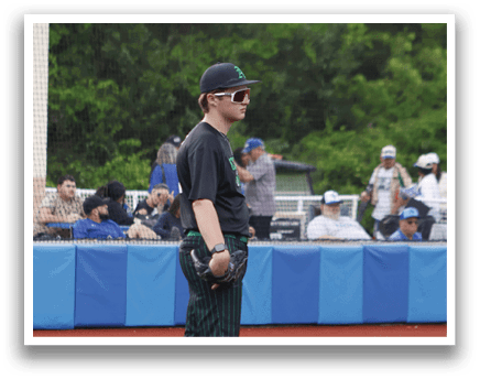 A baseball player wearing a black shirt and green pants standing on the pitcher's mound. Description generated by AI
