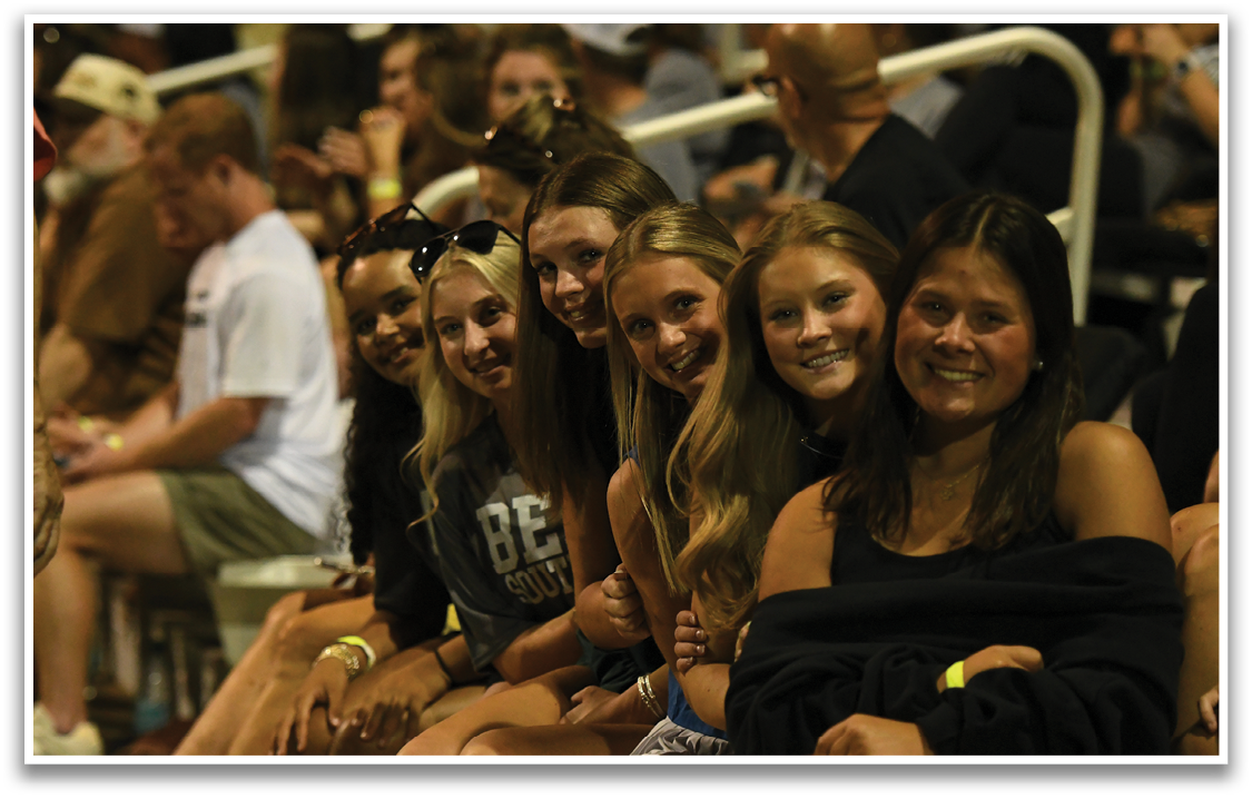 A group of girls sitting in the bleachers. Description generated by AI