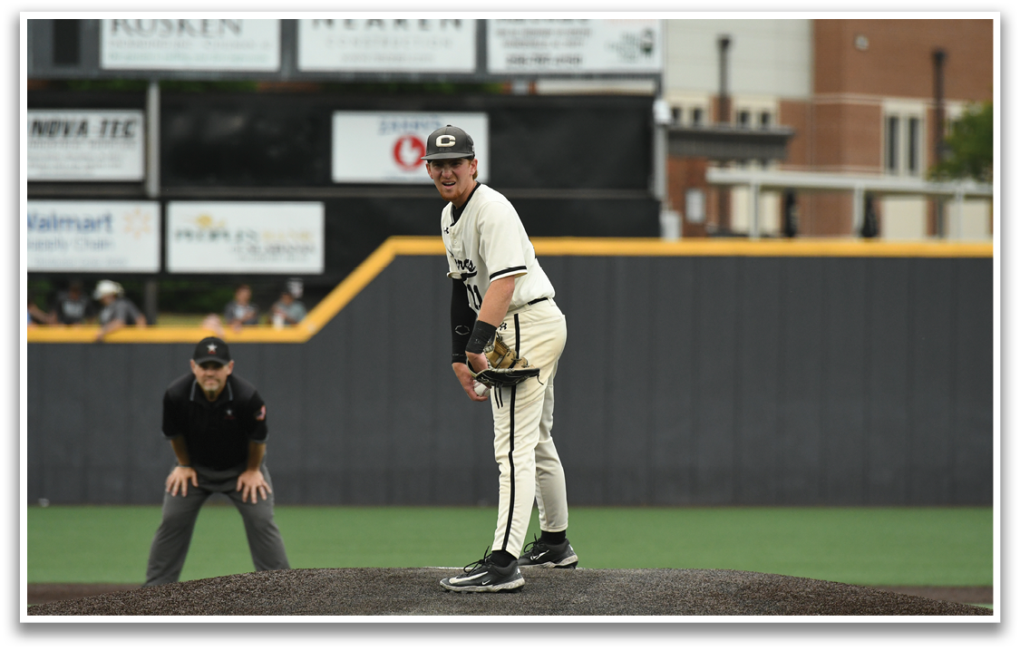 A baseball player in a white and black uniform is standing on a pitcher's mound. Description generated by AI