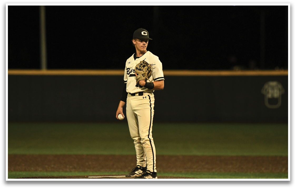 A baseball player wearing a white and black uniform stands on a field. Description generated by AI