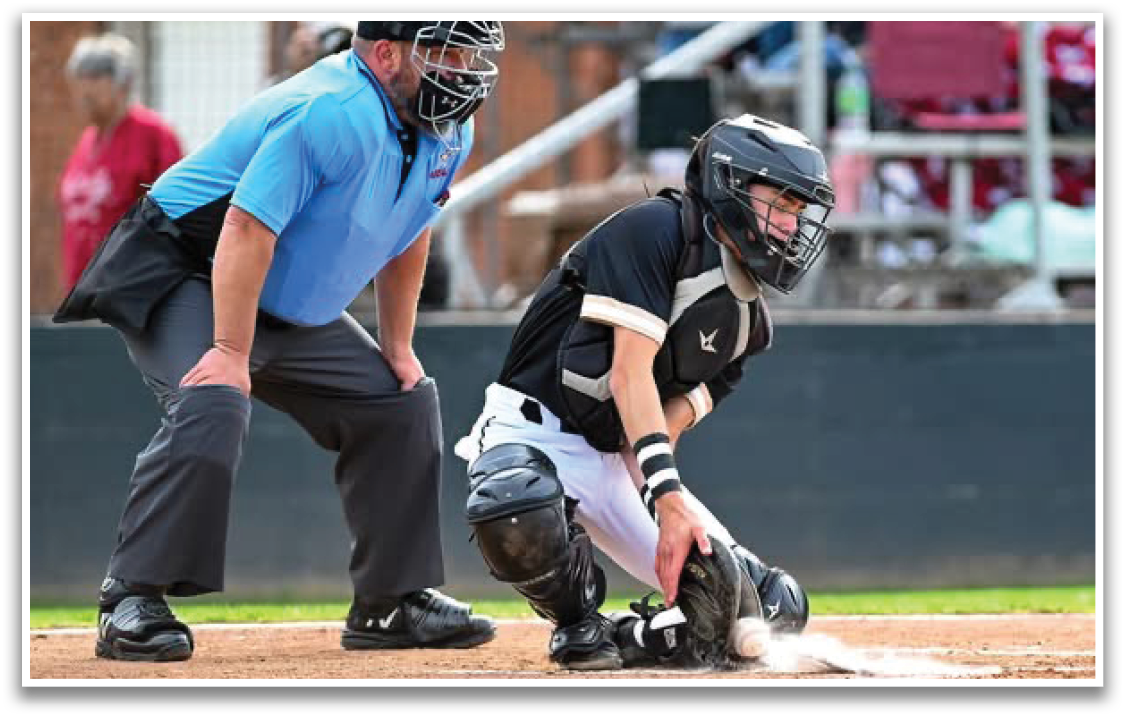 A baseball catcher wearing a black helmet and white pants. Description generated by AI