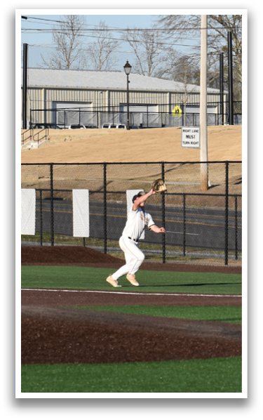 A baseball game is taking place on a field with a man standing on the pitcher's mound, preparing to throw the ball. There are several other people on the field, some of them wearing baseball gloves. A truck is parked in the background, and a bench is visible in the distance. AI generated content