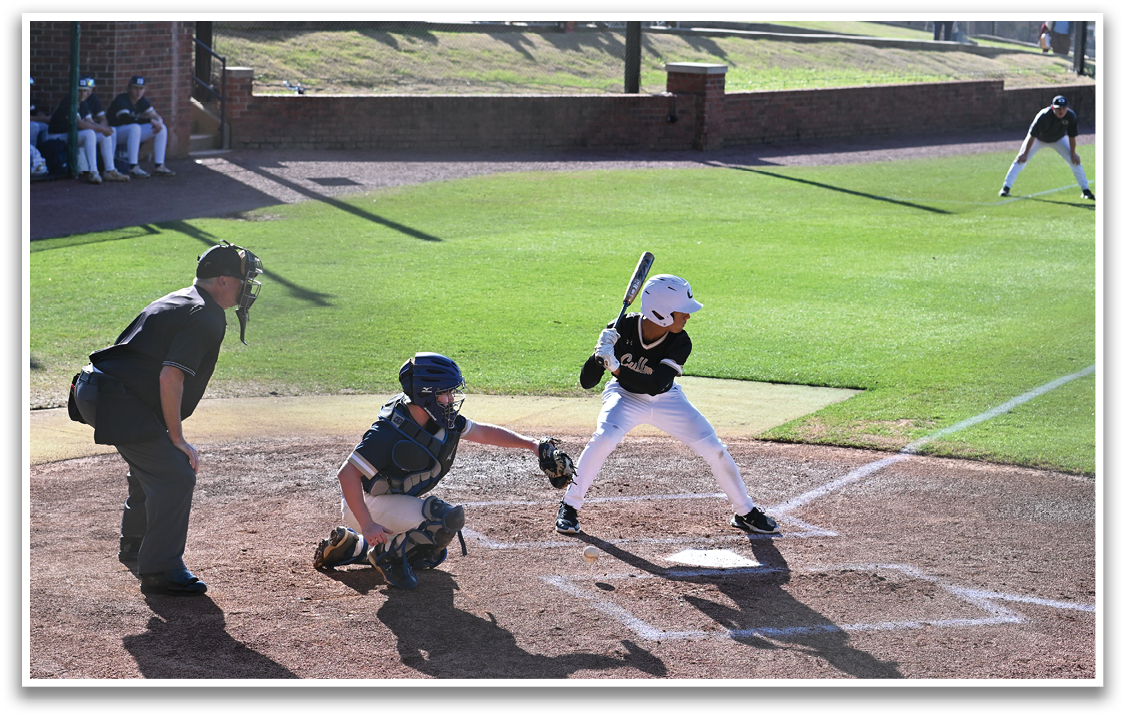 A baseball player is at home plate, holding a bat and preparing to swing. The catcher is positioned behind him, wearing a baseball glove. There are several other people in the scene, some of whom are standing and others sitting on chairs. The overall atmosphere appears to be that of a baseball game in progress. AI generated content