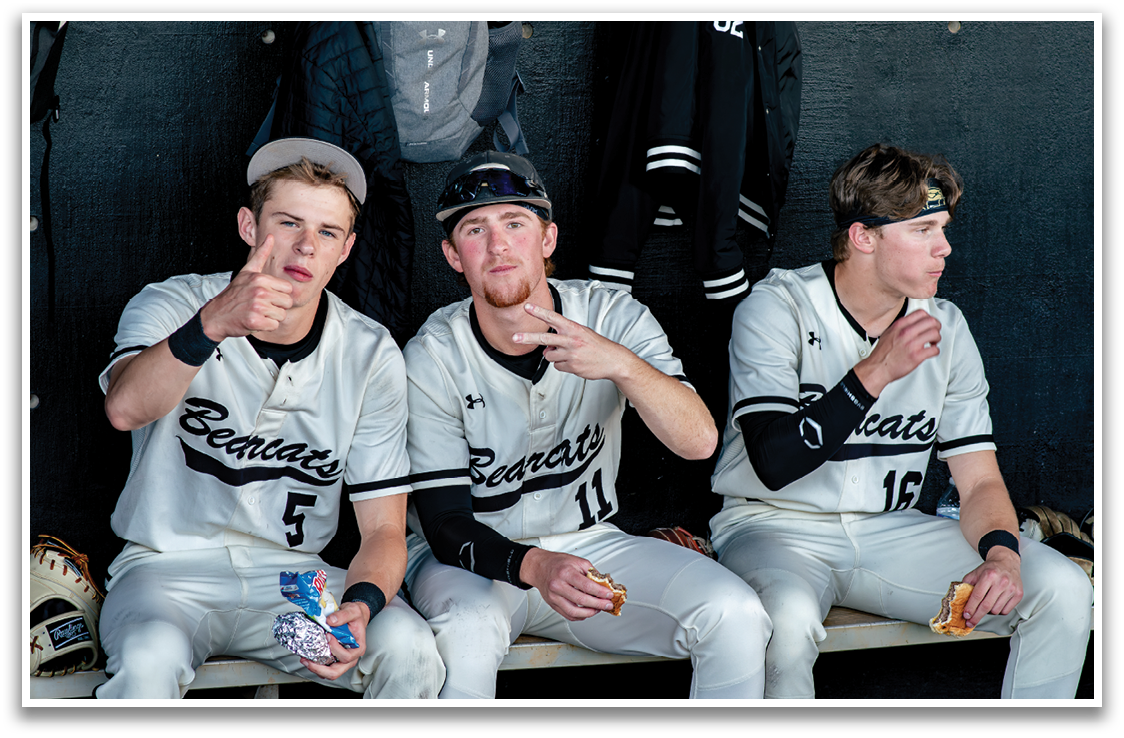 Two baseball players are sitting on a bench, one pointing at the other. They are wearing uniforms and are likely taking a break during a game. AI generated content