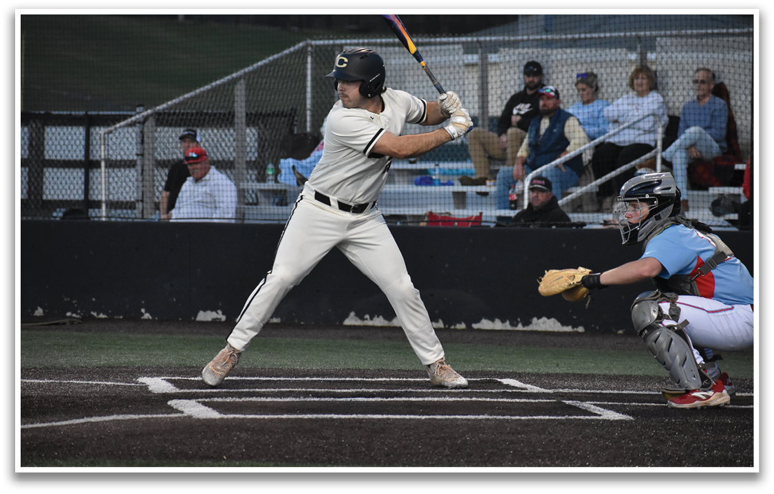 A baseball player in a white uniform is swinging a bat, attempting to hit a ball. The player is wearing a helmet for protection. There are several other people in the scene, some of whom are sitting on a bench, and others are standing. A baseball glove is visible in the scene, likely belonging to the catcher. AI generated content