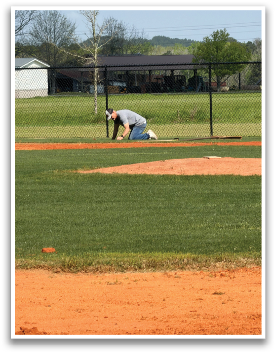 A man is bending over on a baseball field, possibly fixing a base. AI generated content