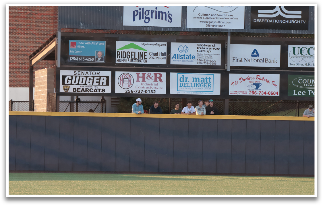 A group of people are sitting on a bench in front of a baseball field. AI generated content