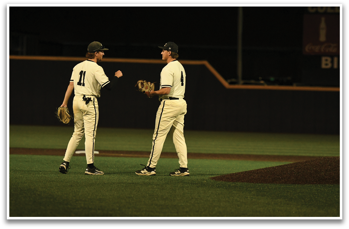 Two baseball players wearing white uniforms and black hats are standing on a field. AI generated content