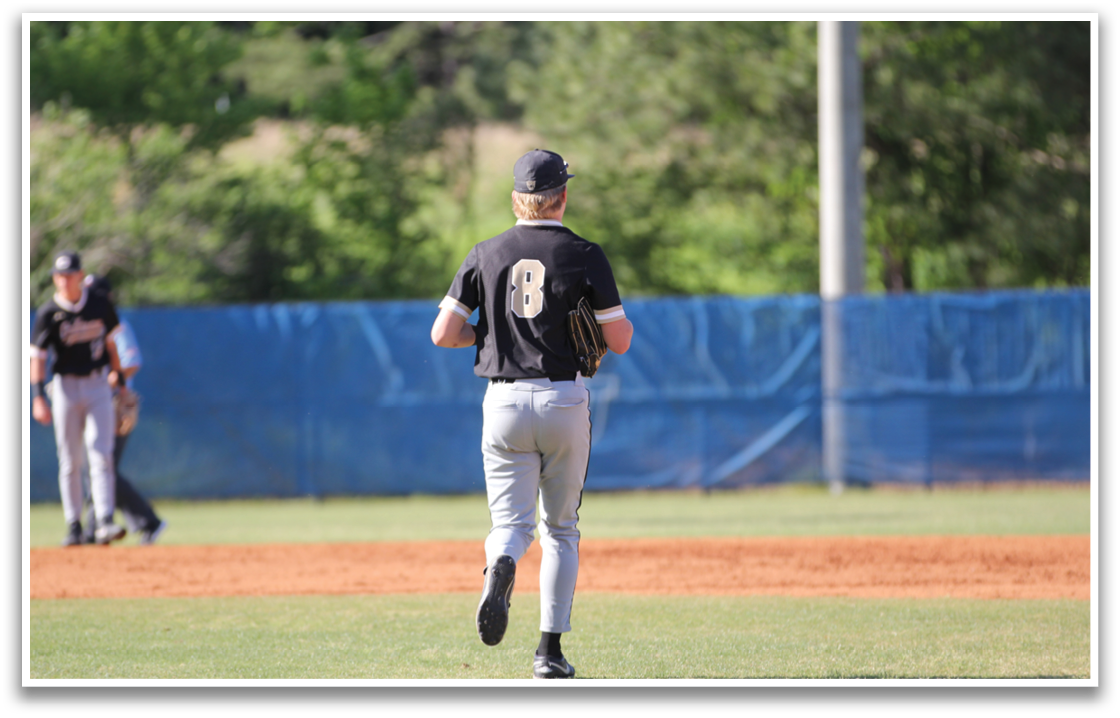 A baseball player wearing a black shirt and grey pants is walking across the field. AI generated content