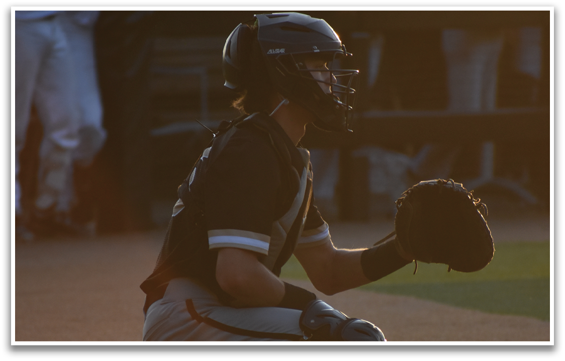 A baseball catcher is sitting on the field, wearing a helmet and a black shirt. AI generated content