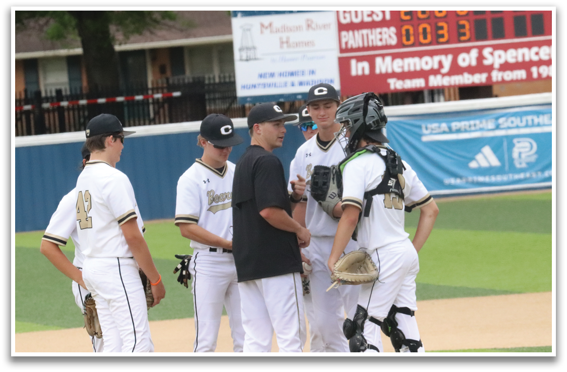A group of baseball players wearing white uniforms are standing on a field. They are engaged in conversation and appear to be discussing their game strategy. One player is holding a cell phone, possibly checking the score or communicating with a teammate. The scene is set on a baseball field with a scoreboard visible in the background. AI generated content