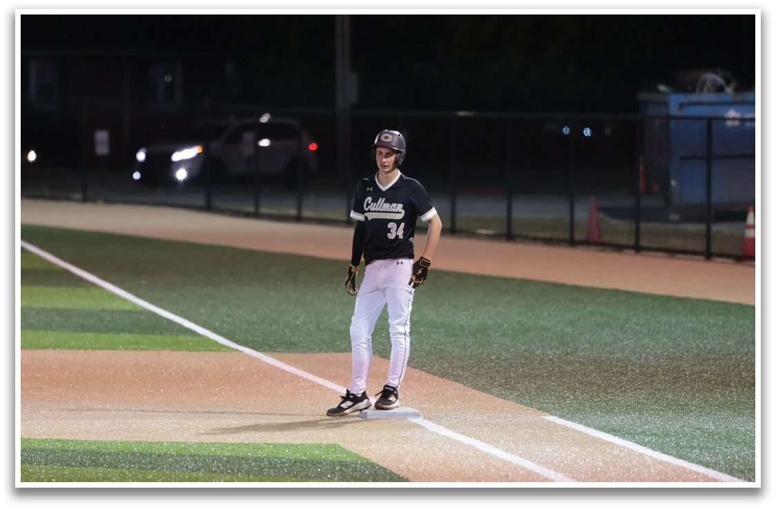 A baseball player stands on the field, wearing a black shirt and white pants. He is holding a baseball bat and appears to be waiting for the next play. AI generated content
