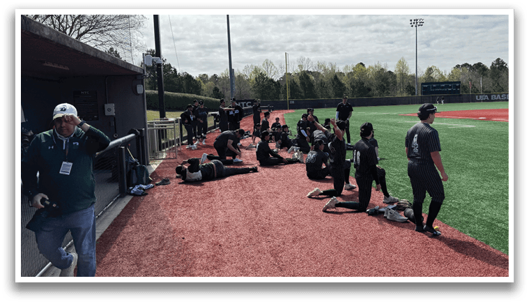 A baseball field with a group of people sitting on the side. Description generated by AI