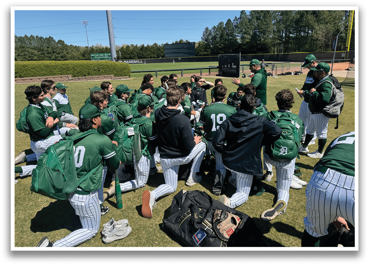 A group of baseball players in green and white uniforms are sitting on the grass. Description generated by AI