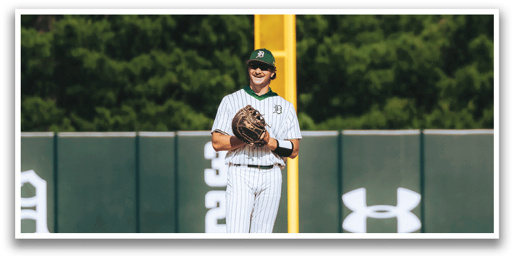 A baseball game is taking place with a man in a black shirt and gray pants standing behind a catcher. Description generated by AI