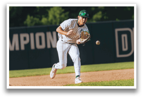 A baseball player in a black shirt and black socks is bending over to catch a ball. Description generated by AI