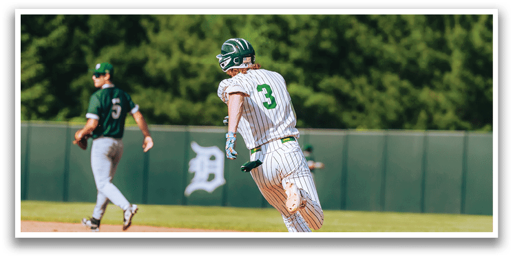A baseball game is taking place with a man in a black shirt and gray pants standing behind a catcher. Description generated by AI