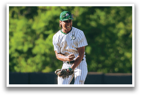 A baseball player in a black shirt and black socks is bending over to catch a ball. Description generated by AI