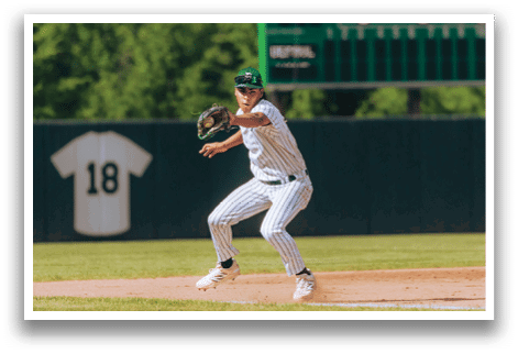A baseball player in a black shirt and black socks is bending over to catch a ball. Description generated by AI