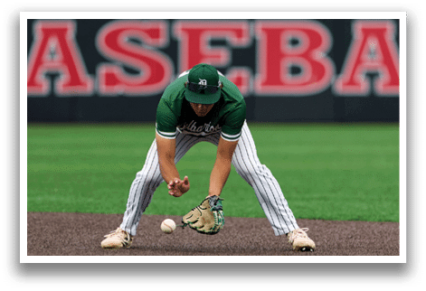 A baseball player in a black shirt and black socks is bending over to catch a ball. Description generated by AI