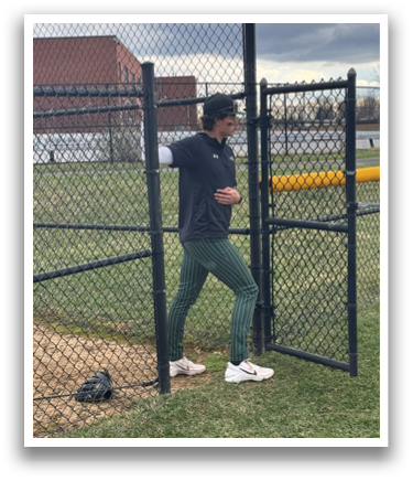 A man wearing a black shirt and green pants is standing in front of a chain link fence. Description generated by AI